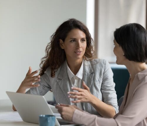 Two,Business,Women,Sit,At,Desk,Discuss,Project,Details,,Diverse