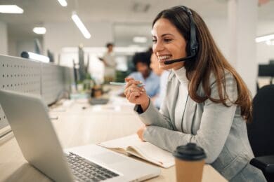 Smiling,Caucasian,Business,Woman,With,Headset,Working,On,A,Laptop